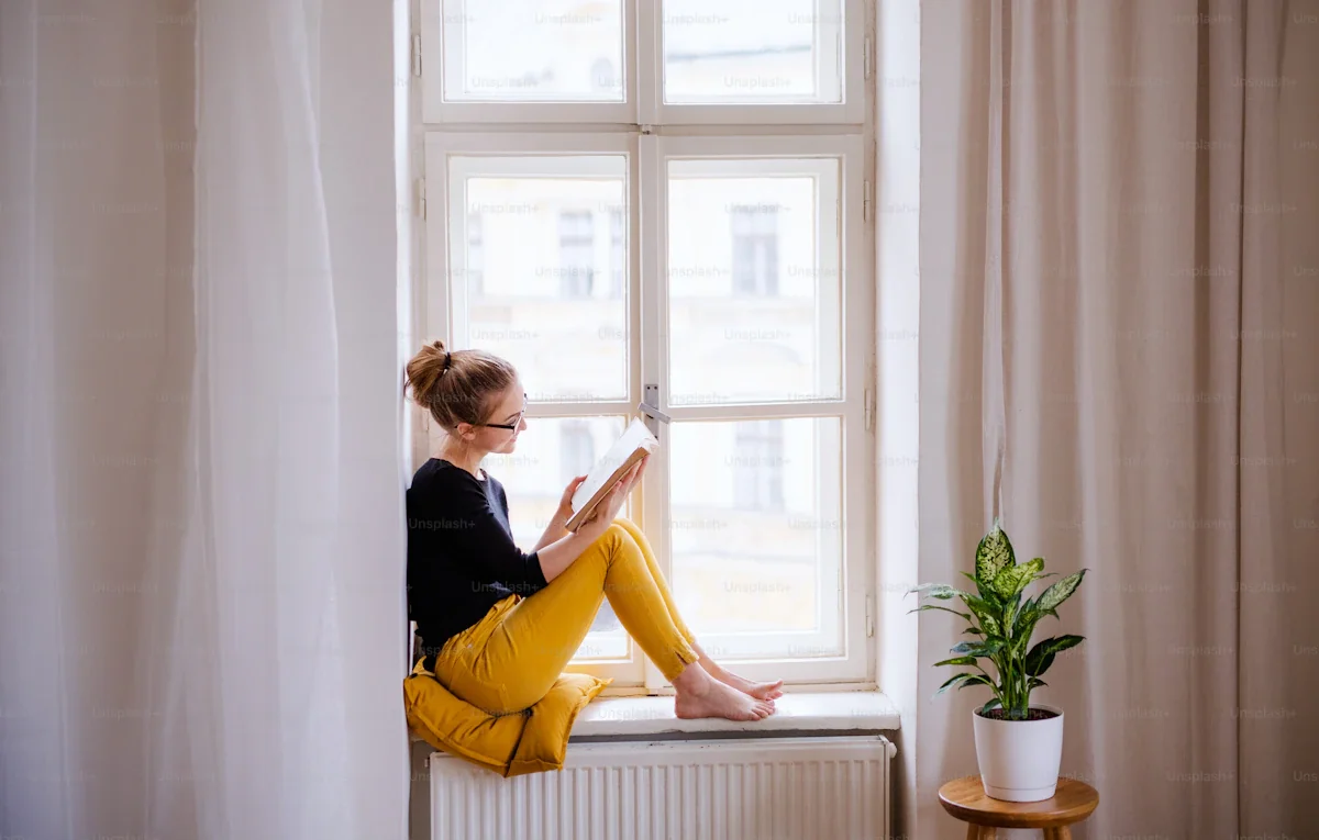 A quiet reading nook with morning light, a worn armchair, a small table with a book and a cup, the suggestion of unhurried hours