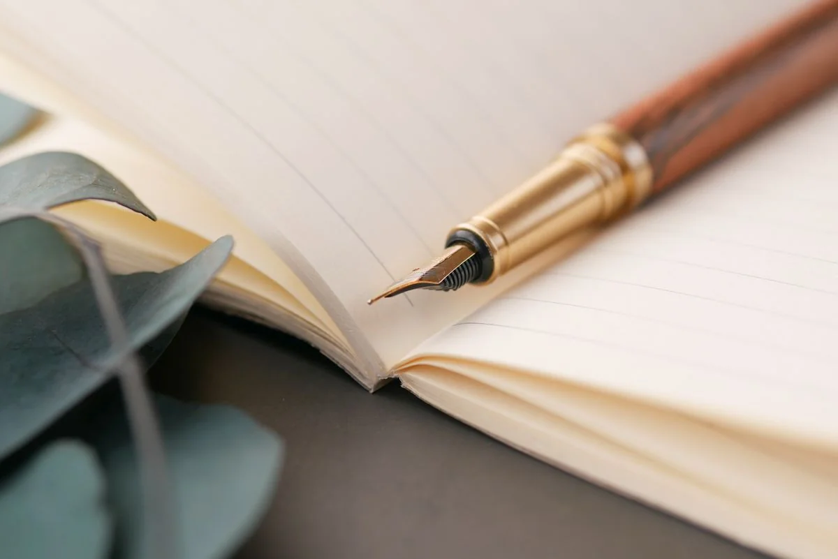 Fountain pen resting on a worn leather journal, warm desk lamp light, a letter half-written