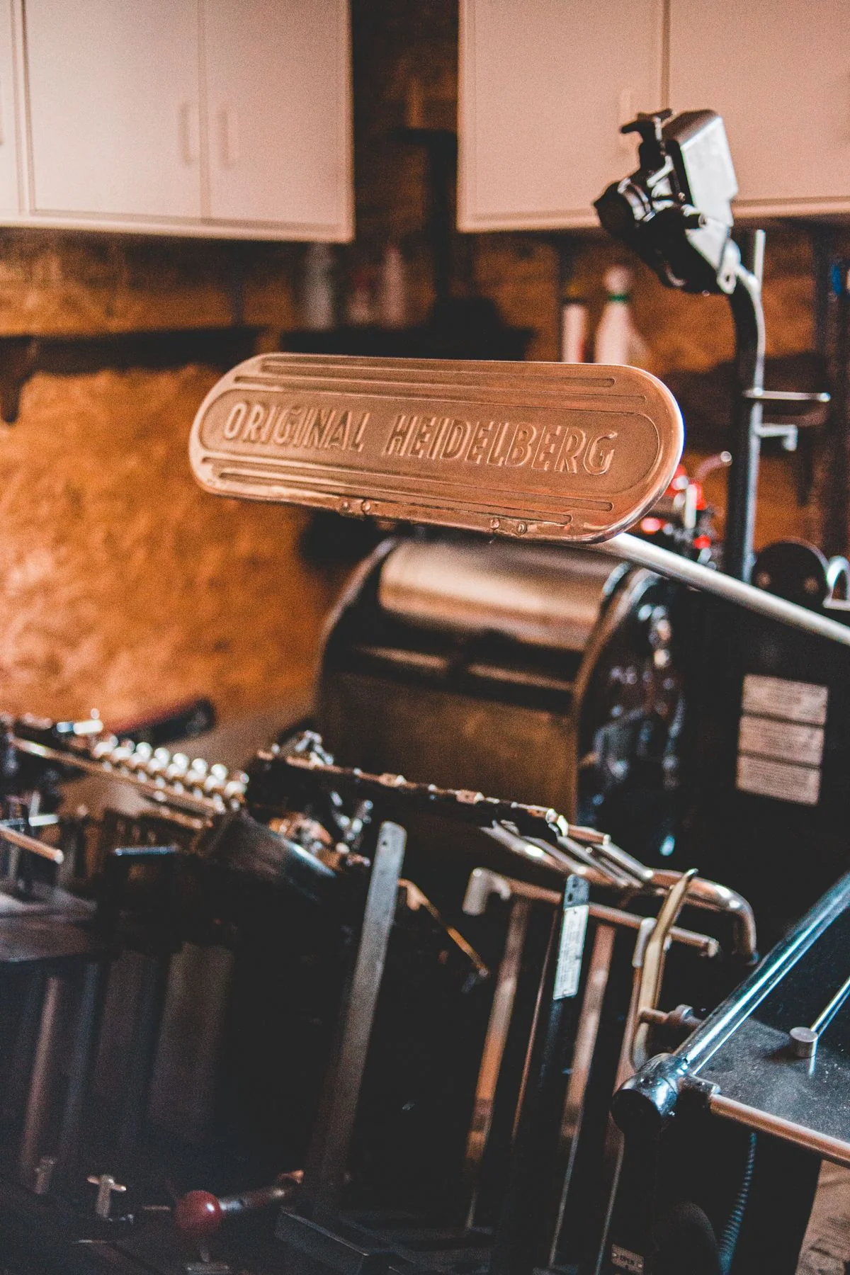 A vintage brass letter press with embossed letters, warm afternoon light catching the raised type — the machine that makes its mark and forgets the making