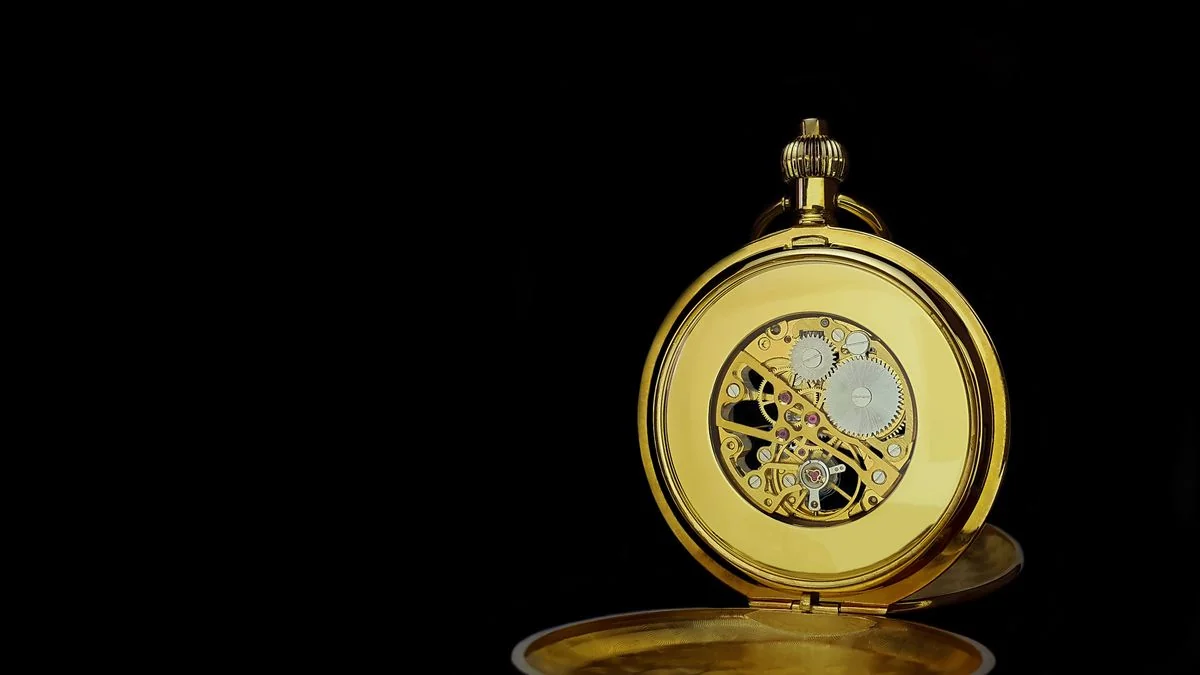 An open pocket watch showing intricate mechanical movement, gears and springs visible in warm afternoon light — time kept by mechanism, not by memory