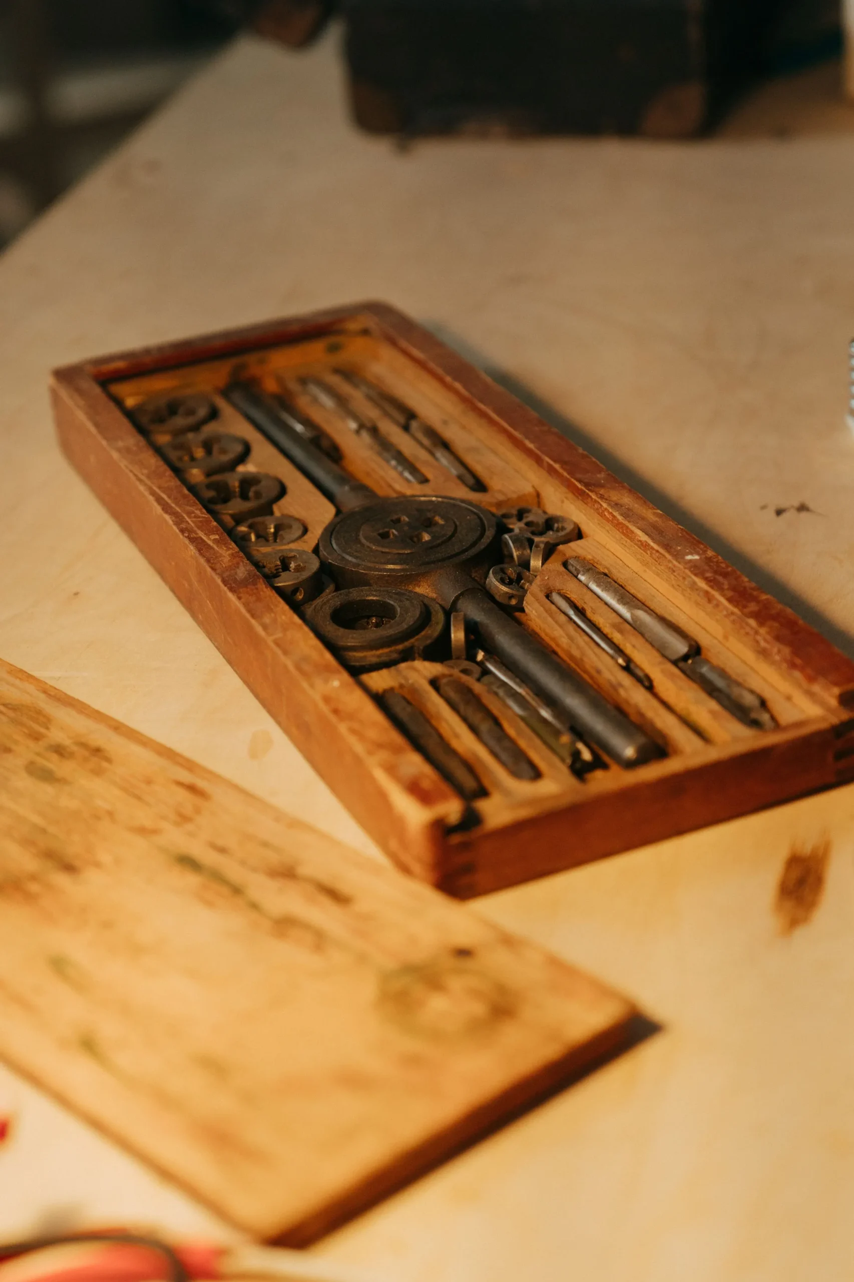 A worn wooden workshop table with brass tools arranged with care — every tool patient, every surface marked by ten thousand uses