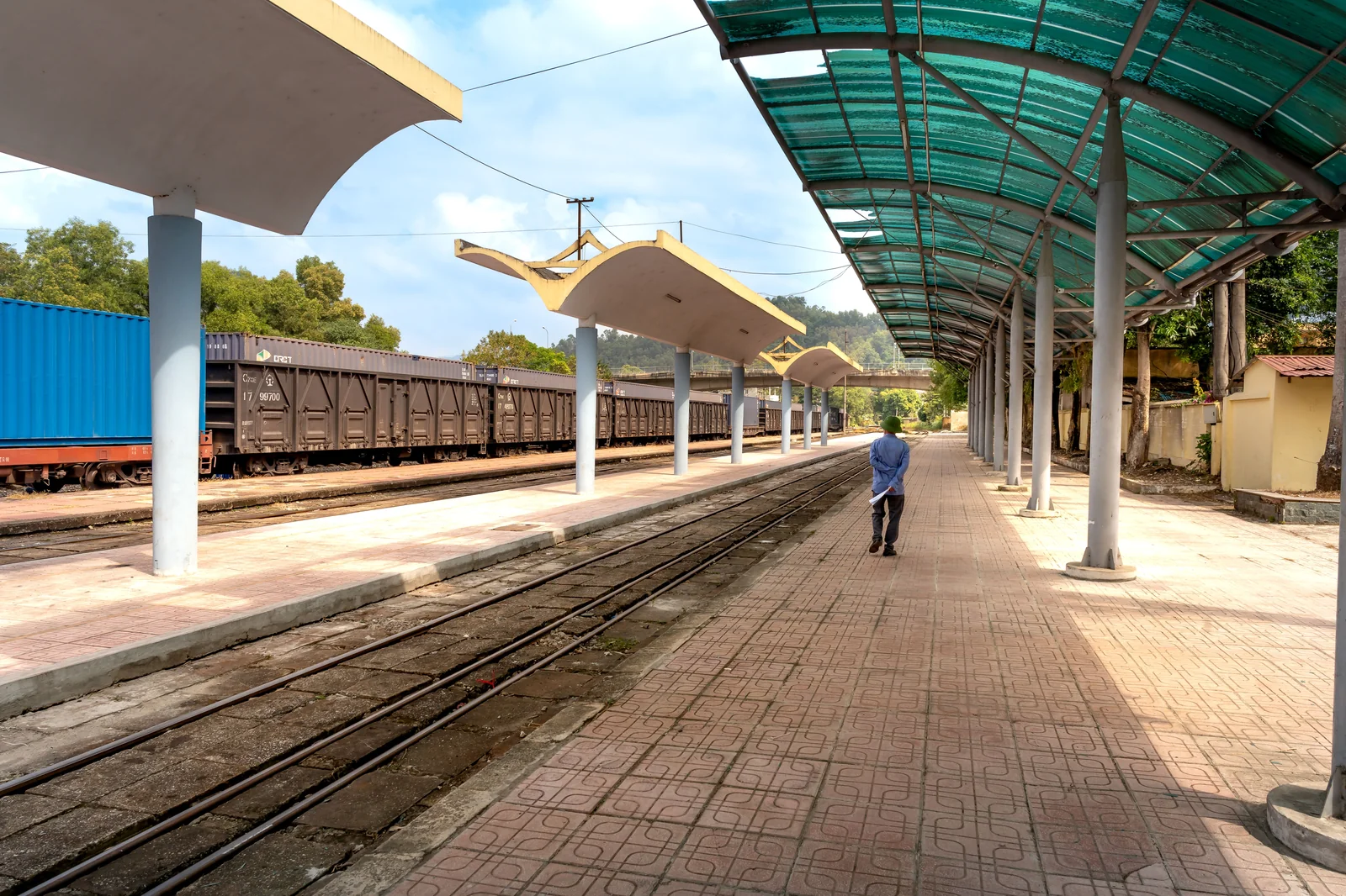 A solitary figure stands on an empty train platform, waiting for a train in the early morning — the geometry of patience made spatial