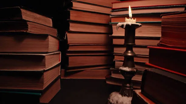 Single candle flame in a dark room surrounded by unseen shelves