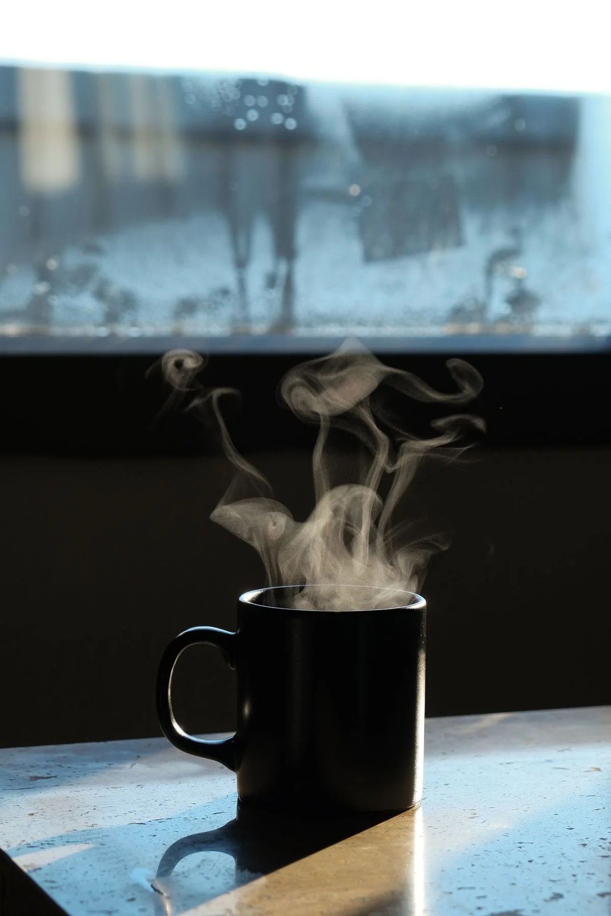 A steaming cup of coffee on a windowsill, morning sunlight pooling on the wood around it