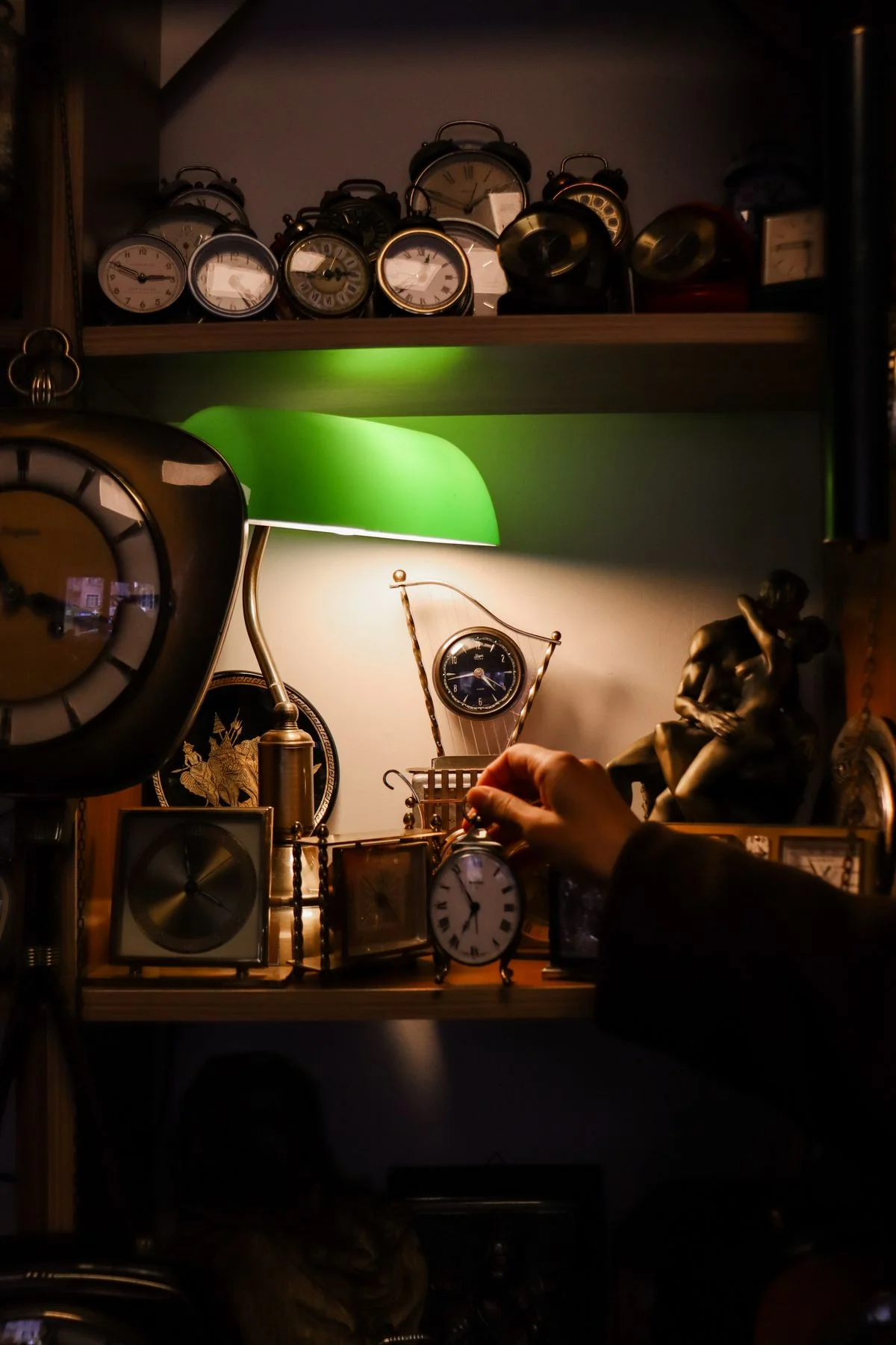 A collection of antique clocks of varying sizes, displayed on a wooden shelf in warm, dim light