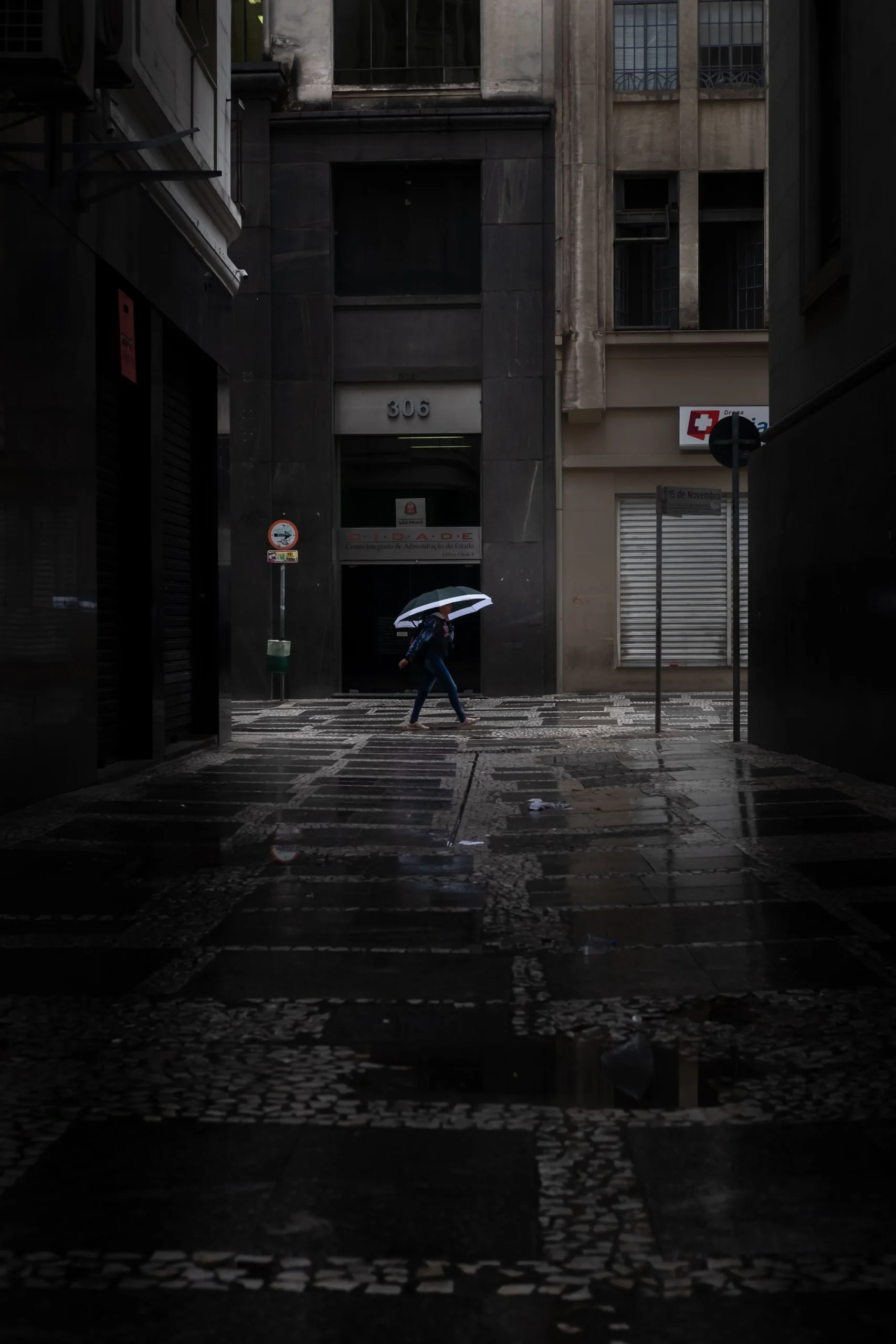 A person walking with an umbrella in a dark, rainy alley, alone in the urban night