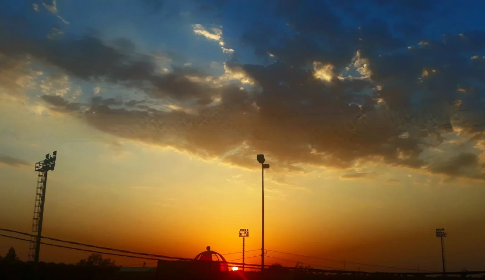Dramatic sunset over industrial floodlights — the end of the day, the end of a mechanism